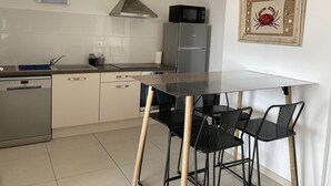 Eine moderne Küche mit weißen Schränken, einem Edelstahl-Geschirrspüler, einer Mikrowelle und einem Gasherd. Ein Holztisch wird von zwei schwarzen Stühlen begleitet.