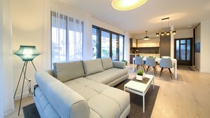 A modern living room with a sectional sofa, a dining area with chairs, and a kitchen in the background.