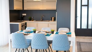A modern kitchen with white cabinets, a black pendant light, and a dining area with a white table and blue chairs.