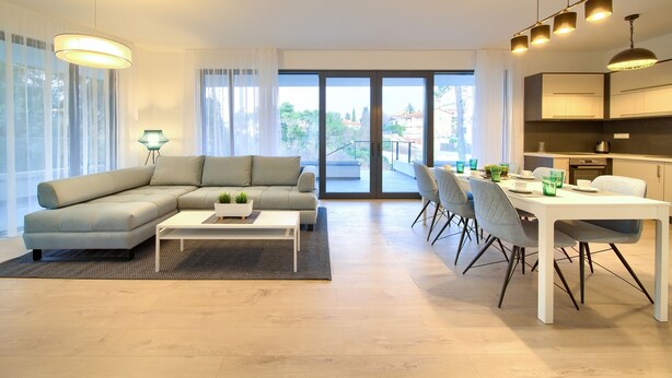 A modern living room with a sectional sofa, a dining table with chairs, and a kitchen area with pendant lighting.