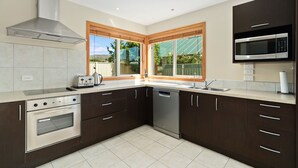 Une cuisine moderne avec des meubles en bois foncé, des appareils électroménagers en acier inoxydable et une fenêtre équipée de stores.