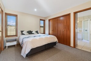 Quarto com cama, guarda-roupa, banheiro com chuveiro de vidro e janela com persianas.