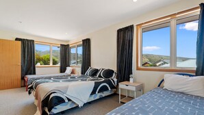 Une chambre avec deux lits, une porte en bois, une fenêtre avec des rideaux et une vue sur les collines.