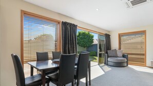 Un coin repas comprenant une table et des chaises, un canapé et une porte-fenêtre coulissante donnant sur un jardin.