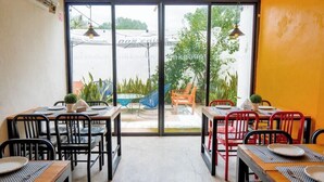 Un restaurante con mesas y sillas, un separador de vidrio y vistas a un jardín y una zona de estar al aire libre.