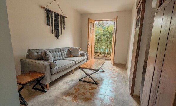 A living room with a grey sofa, a wooden coffee table, and a geometric patterned floor. - Habitación con 2 camas matrimoniales y alberca privada en el centro de Mérida. (Mérida)
