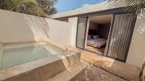 Un área de piscina moderna al aire libre con un jacuzzi, un dormitorio con cama y cortinas, y un ventanal corredero que da al dormitorio.