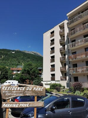 A multi-story building with balconies, a sign indicating private parking, and a mountainous backdrop.
