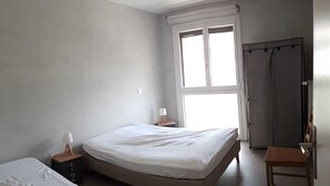 A bedroom with two beds, a window, a curtain, a nightstand, and a chair. - T4 apartment in the heart of Briançon, 400 m from the Serre-Chevalier slopes (Briançon)