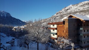 A modern multi-story building with a wooden facade and a sloped roof, surrounded by snow-covered trees and mountains in the background. - T4 apartment in the heart of Briançon, 400 m from the Serre-Chevalier slopes (Briançon)