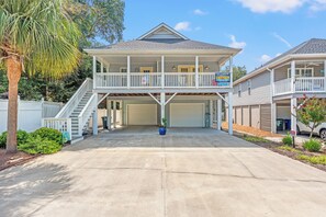 Een tweelaags huis met een overdekte garage, een balkon en een oprit die naar de garage leidt.