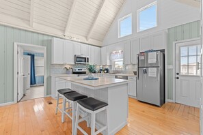 A kitchen with a central island, bar stools, a refrigerator, and a microwave. - Flip Flop Paradise - Unique 4 Bedroom Channel Home in Cherry Grove - Walk to Beach (North Myrtle Beach)