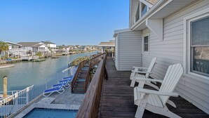 Een pand aan het water met een houten terras, lounge stoelen en een zwembad.