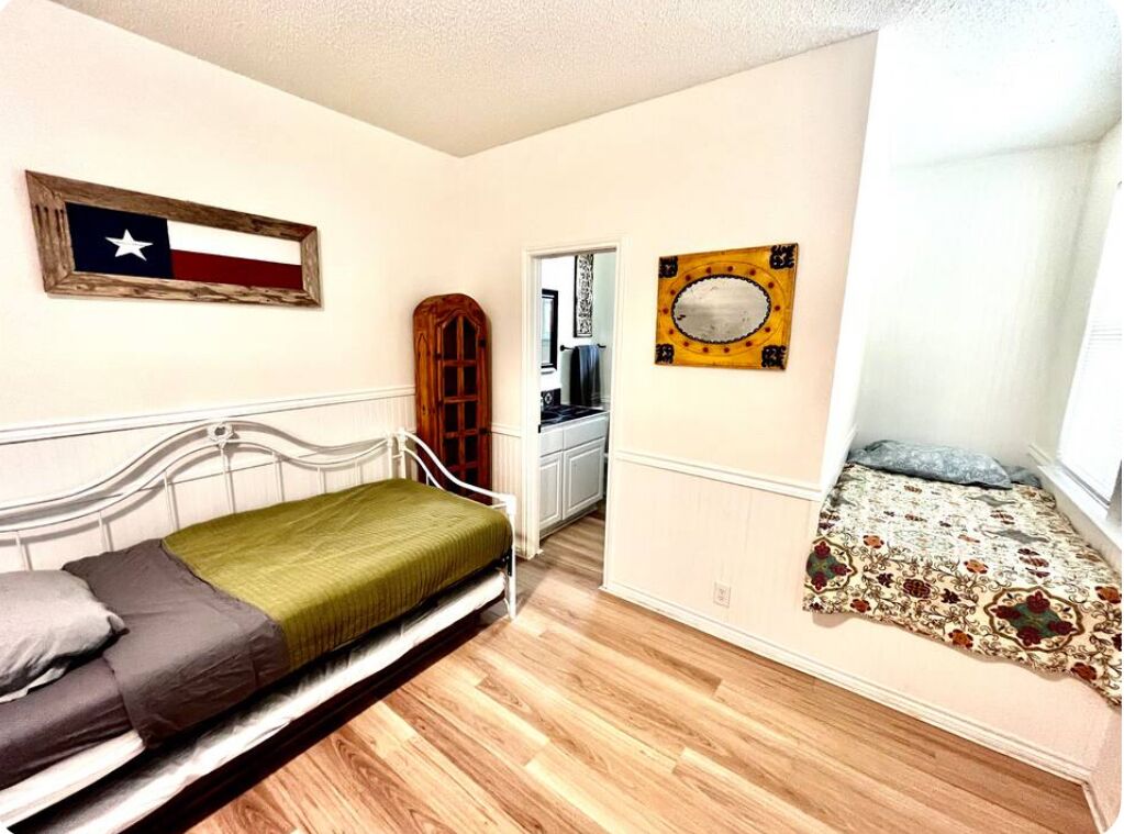 Une chambre avec un lit simple, une armoire en bois, un drapeau du Texas et un miroir décoratif.
