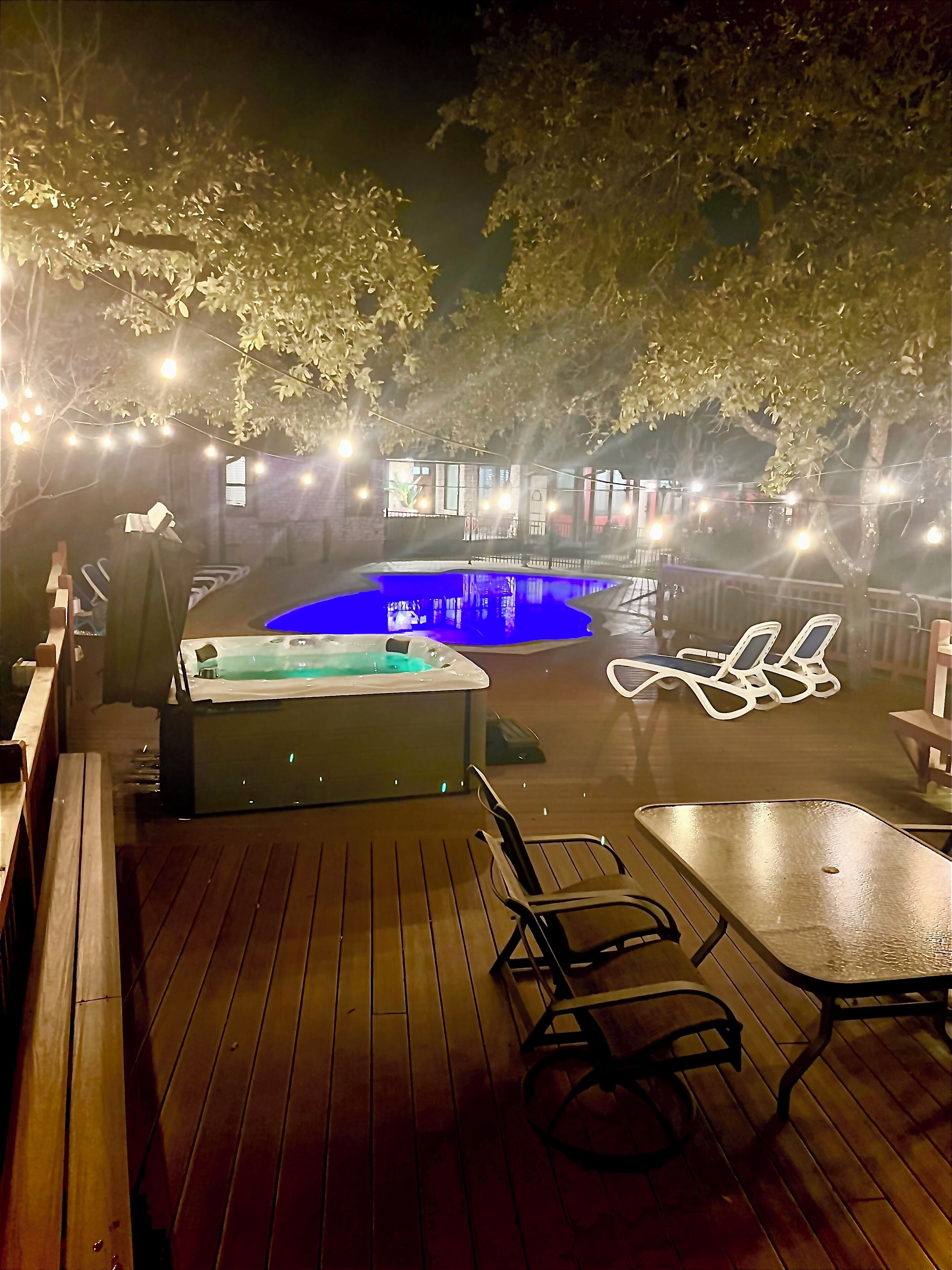 A wooden deck with a hot tub, lounge chairs, and a pool.