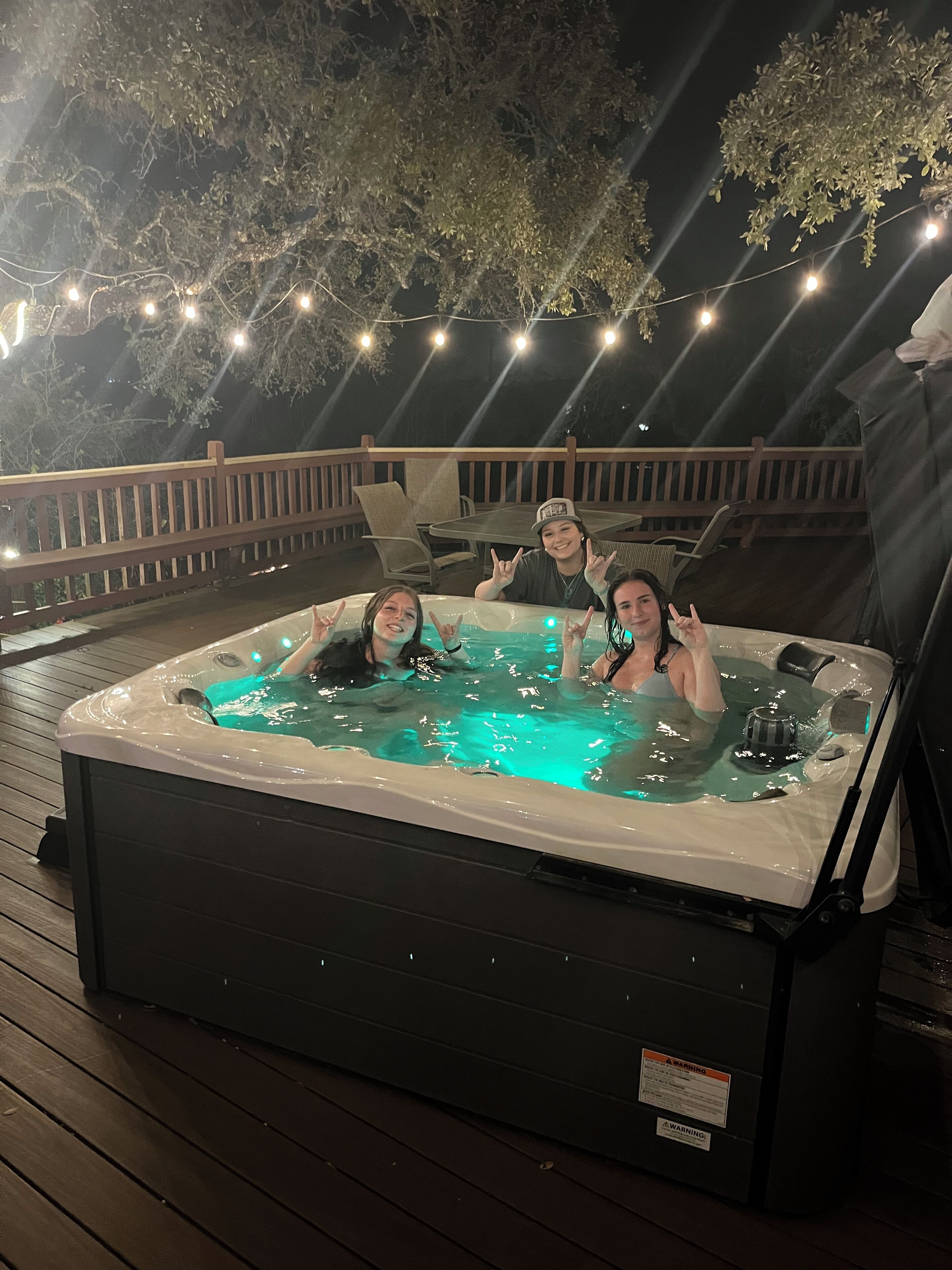 Ett bubbelbad på ett trädäck med ljusslingor ovanför.