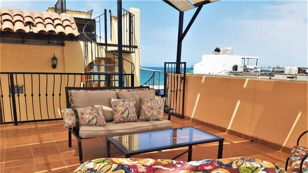 A rooftop terrace with a sofa set, a glass coffee table, and a view of the sea. - Charming 1-Bedroom Loft in Old Port – Rooftop Views, BBQ Area & Steps to Malecon! (Puerto Peñasco)