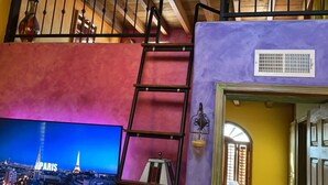 A room with a staircase, a television displaying a cityscape, and a door leading to another room. - Charming 1-Bedroom Loft in Old Port – Rooftop Views, BBQ Area & Steps to Malecon! (Puerto Peñasco)