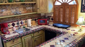 A kitchen with a tiled backsplash, wooden cabinets, a red microwave, a coffee maker, and a sink. - Charming 1-Bedroom Loft in Old Port – Rooftop Views, BBQ Area & Steps to Malecon! (Puerto Peñasco)