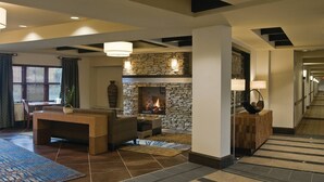 A modern lobby with a stone fireplace, a seating area with a coffee table, and a hallway with a patterned carpet.