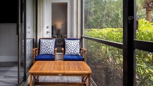 Un balcon avec deux chaises et une table, une porte donnant sur une pièce intérieure, et une vue sur un jardin luxuriant.