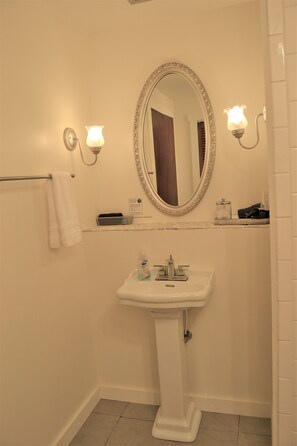 Une salle de bain avec un lavabo sur colonne, un miroir doté d’un cadre orné et deux appliques murales.