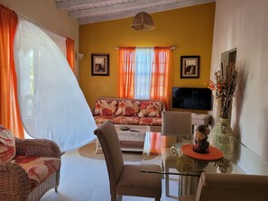 Un salon avec un canapé, des fauteuils, un téléviseur et un vase contenant des fleurs séchées.