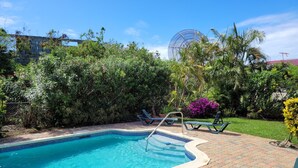 A swimming pool with a tiled edge, surrounded by a brick patio, and various plants and trees in the background. - Relaxing, Amazing beach, pool, Cheap cars, quiet area, surfers paradise 2 (Atlantic Shores)