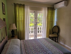Une chambre à coucher comprenant un lit, une chaise, une lampe, une fenêtre avec des rideaux et un climatiseur.