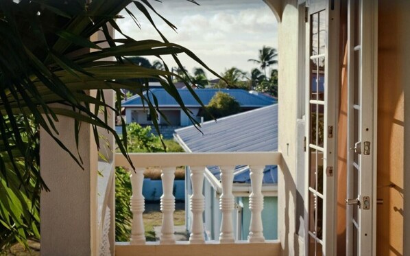 En balkon med hvid gelænder, udsigt over et boligområde med huse og palmer.