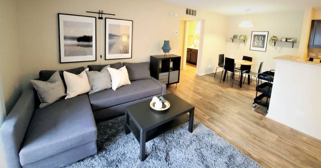 A modern living room with a grey sofa, a black coffee table, and a dining area with a kitchen in the background.