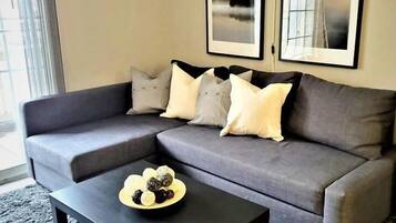 A modern living room with a grey sectional sofa, a black coffee table, and a rug. There are three framed pictures on the wall.