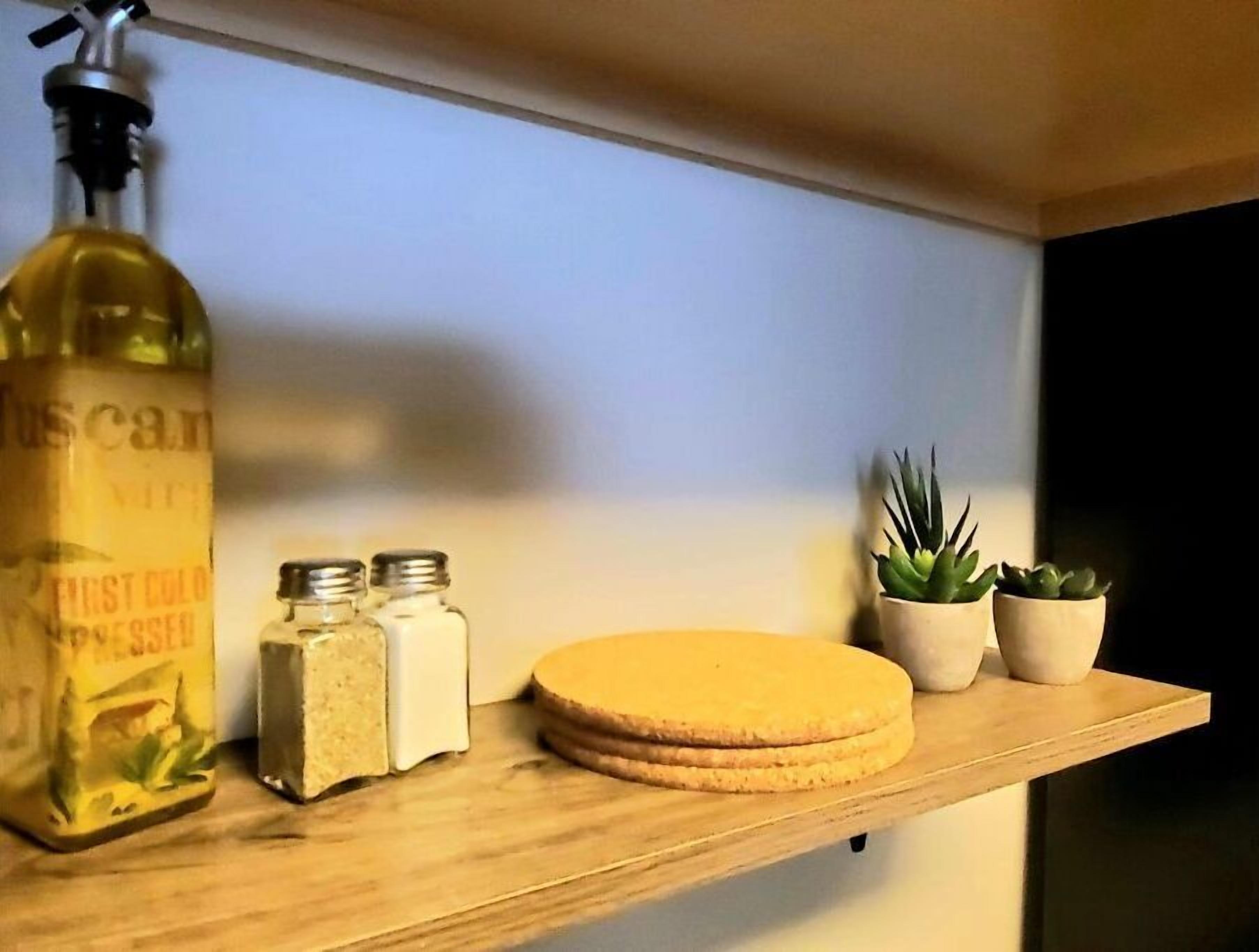 A shelf with a bottle, two jars, and three potted plants.