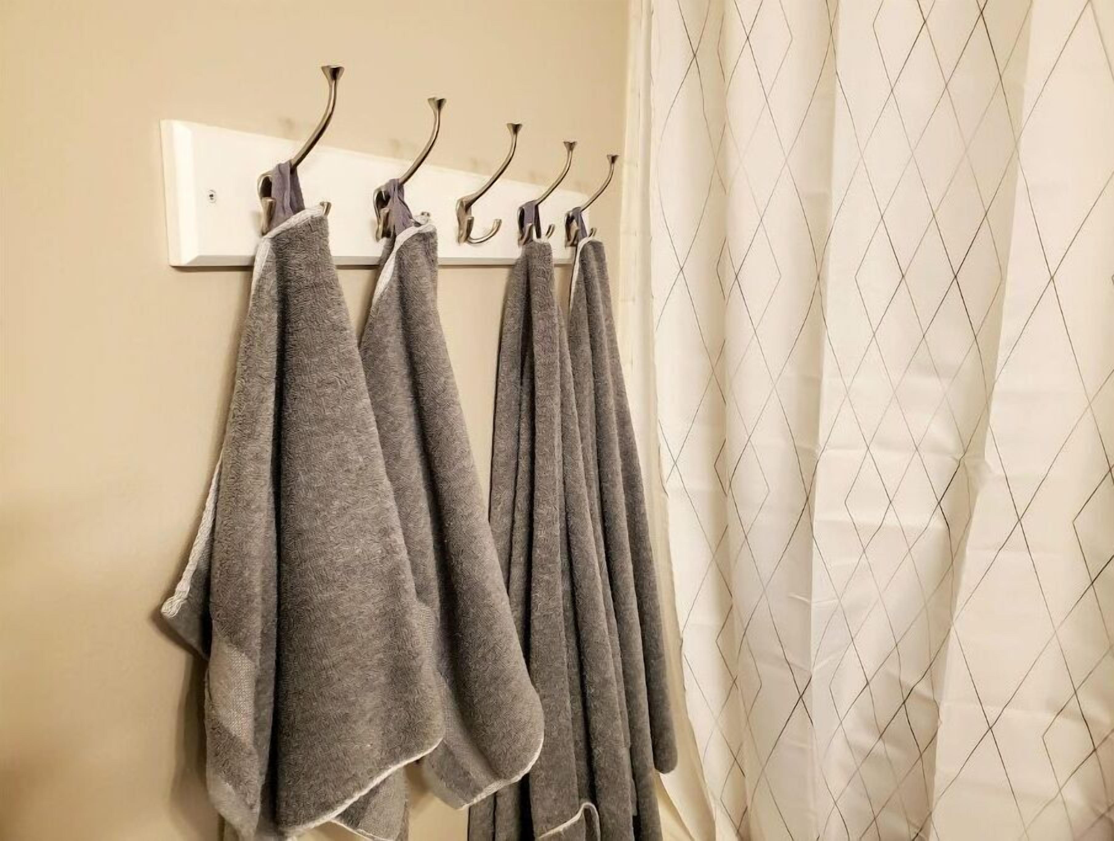 A bathroom with a towel rack holding several towels, a white light switch, and a diamond-patterned shower curtain.