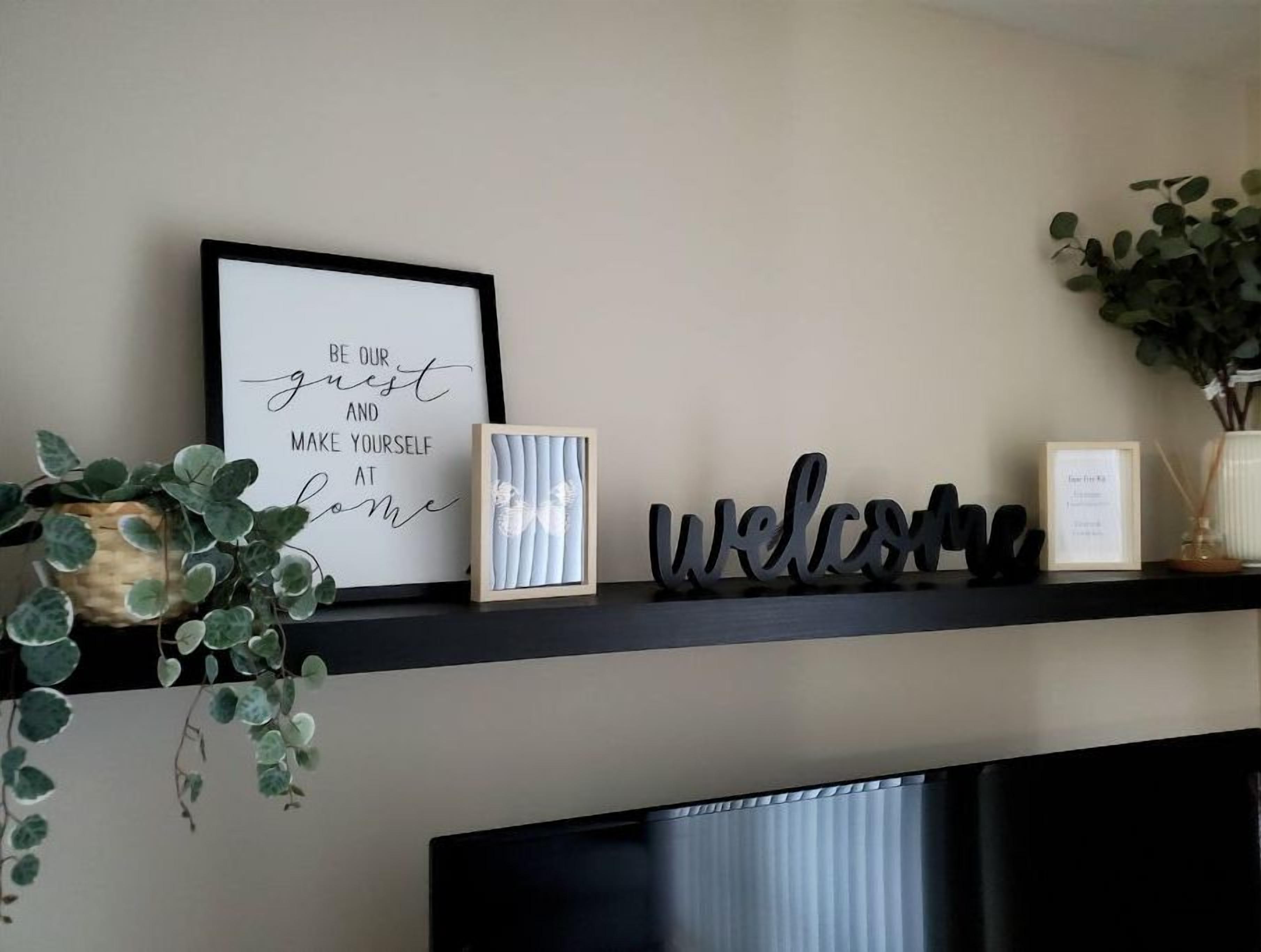 Un letrero en marco con un mensaje de bienvenida, una imagen enmarco y adornos decorativos en una estantería.
