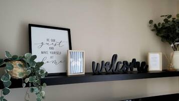 Un letrero en marco con un mensaje de bienvenida, una imagen enmarco y adornos decorativos en una estantería.