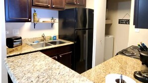 A kitchen with granite countertops, a stainless steel refrigerator, a built-in oven, and wooden cabinets.