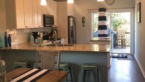 A modern kitchen with white cabinets, a central island with stools, a microwave, and a refrigerator.
