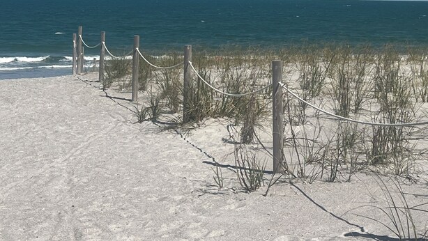 A sandy beach with a wooden fence and rope barrier.