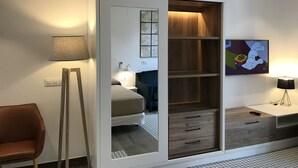 Un dormitorio moderno con armario correderas, una cama, lámparas de noche, un televisor y una silla.