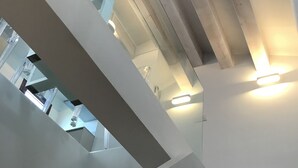 Una escalera moderna con barandilla de vidrio que baja a un nivel inferior con zona de cocina.