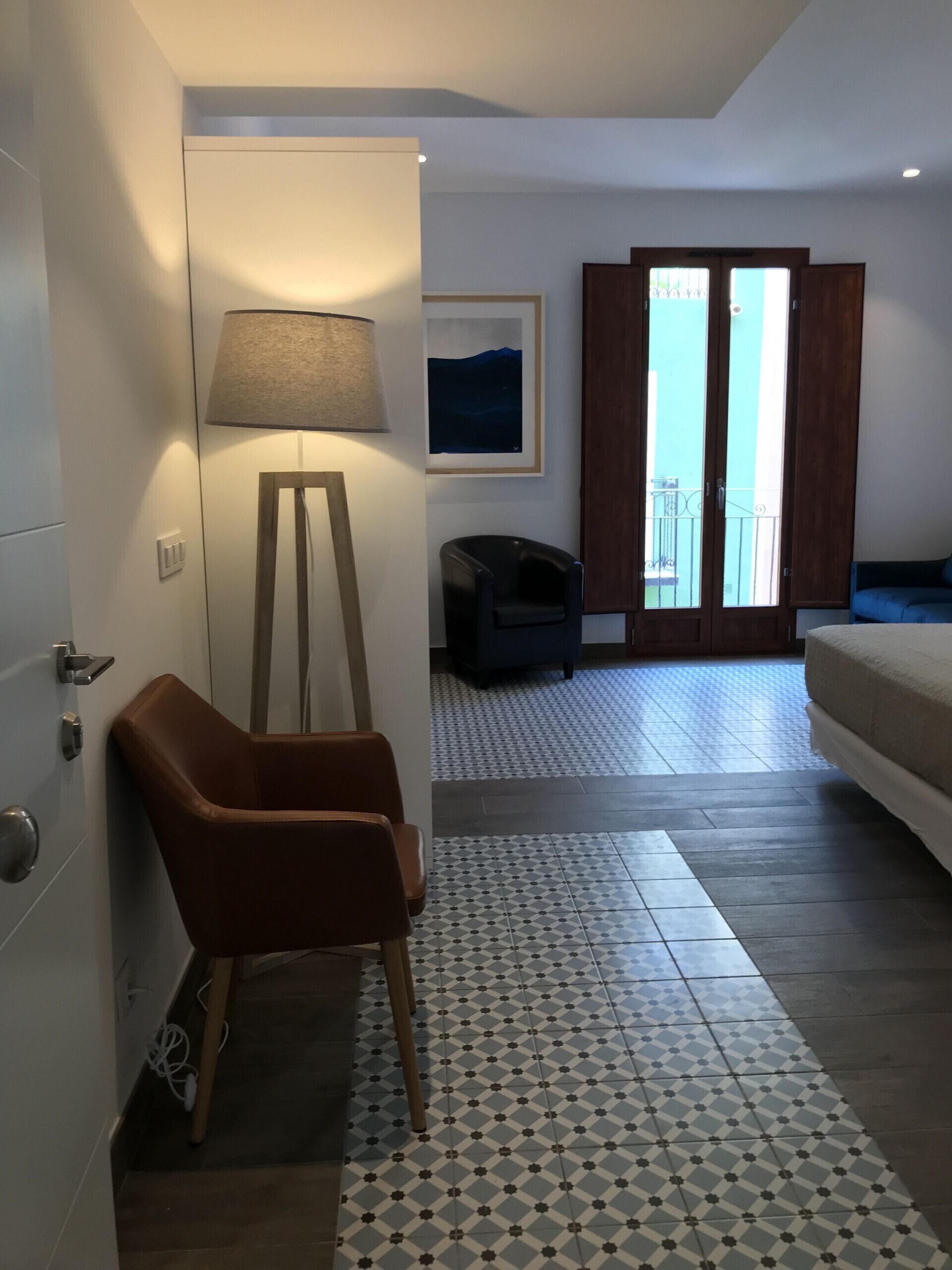 Une chambre moderne avec un fauteuil en cuir marron, un lampadaire, un tableau encadré et un balcon avec vue.