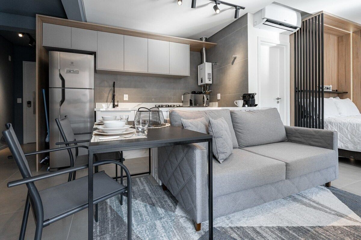 A modern kitchen with grey cabinets, a built-in oven, and a dining area with a grey sofa and table.