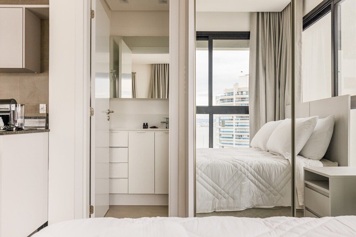 Et moderne hotelværelse med seng, natbord, et lille skrivebord og udsigt til byen gennem store vinduer.