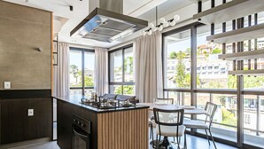 A modern kitchen with a central island, large windows, and a dining area with chairs. - ZEE Studios by Viva - Studios a 200m da beira-mar norte (Florianópolis)