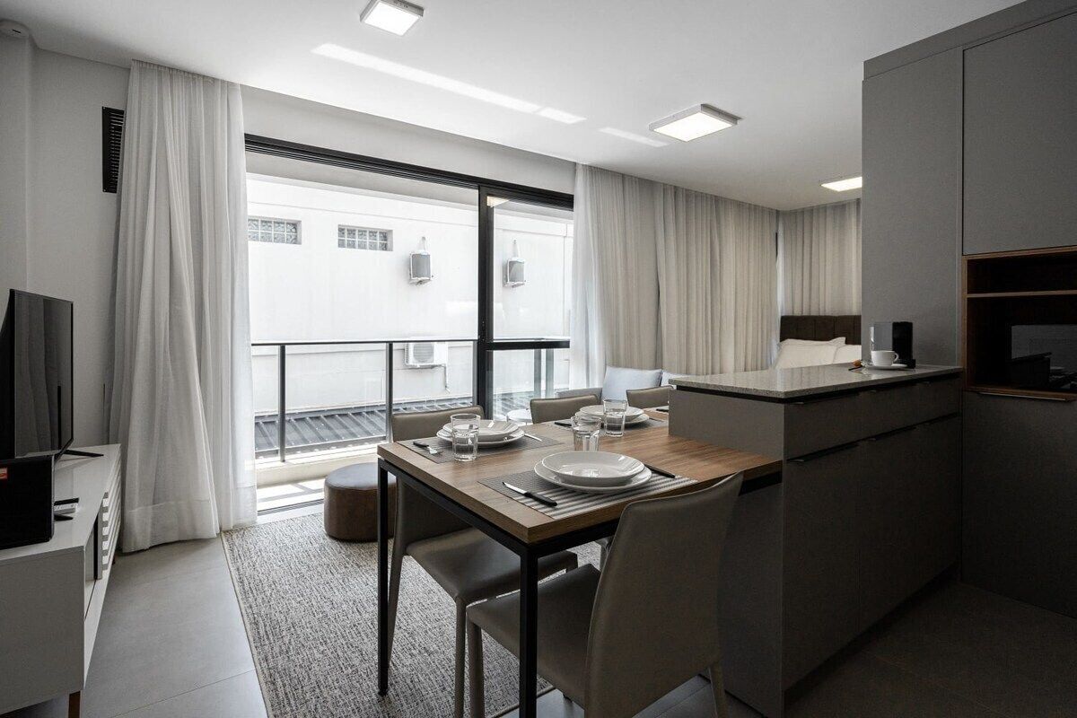 A modern hotel room with a dining area, a kitchenette, and a balcony with curtains.