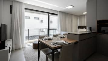 A modern hotel room with a dining area, a kitchenette, and a balcony with curtains.