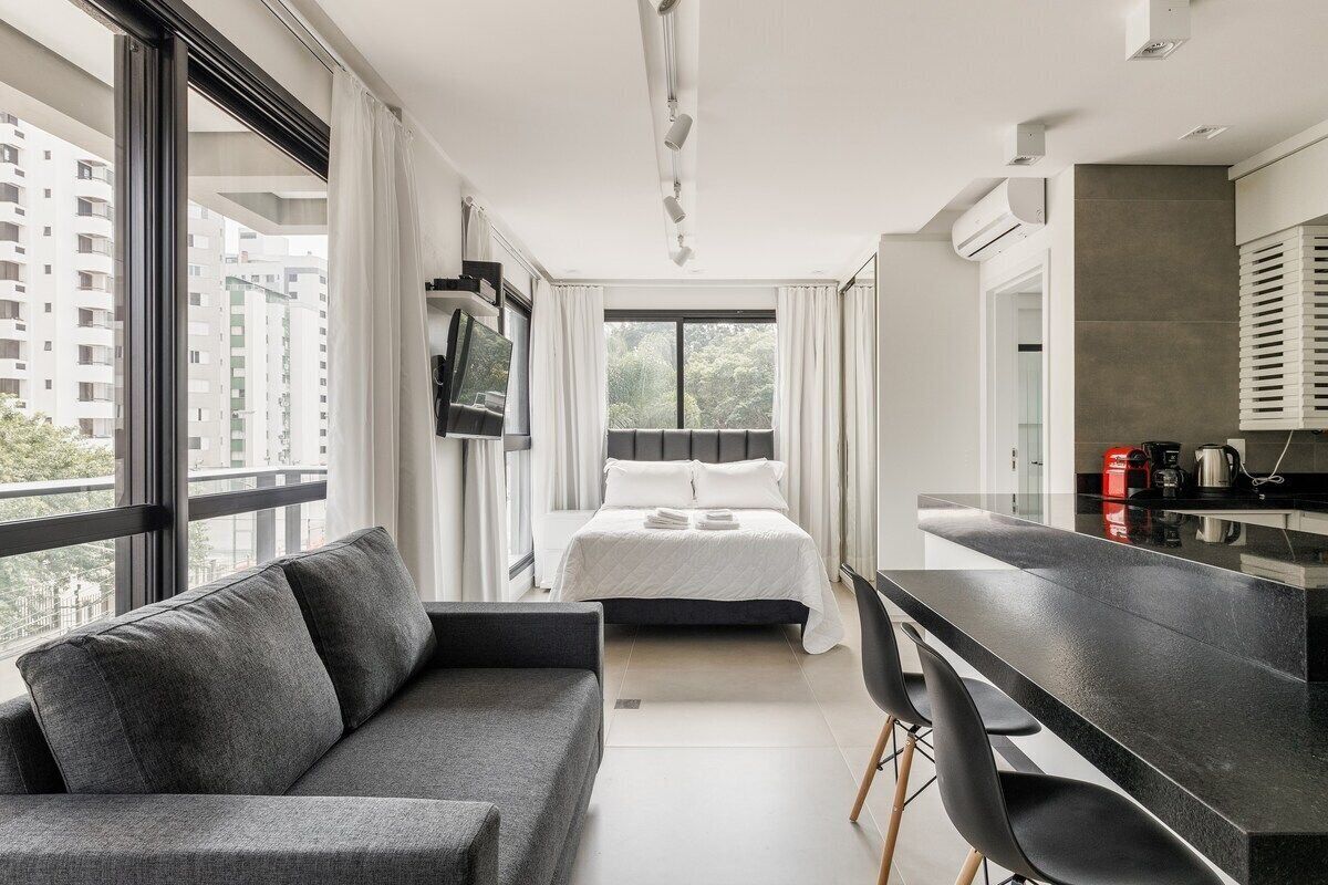 A modern hotel room with a large bed, a sofa, a dining area, and a TV.
