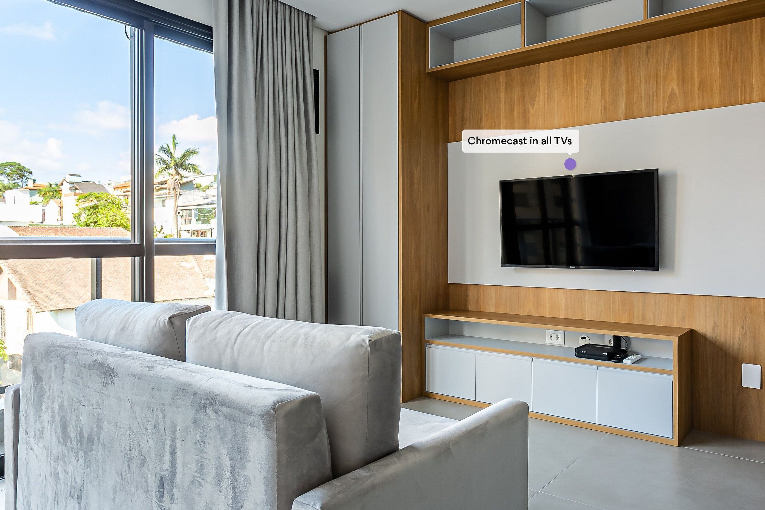 Un salon moderne doté d’une grande fenêtre, d’un téléviseur à écran plat et d’un meuble de rangement intégré pour les appareils multimédias.