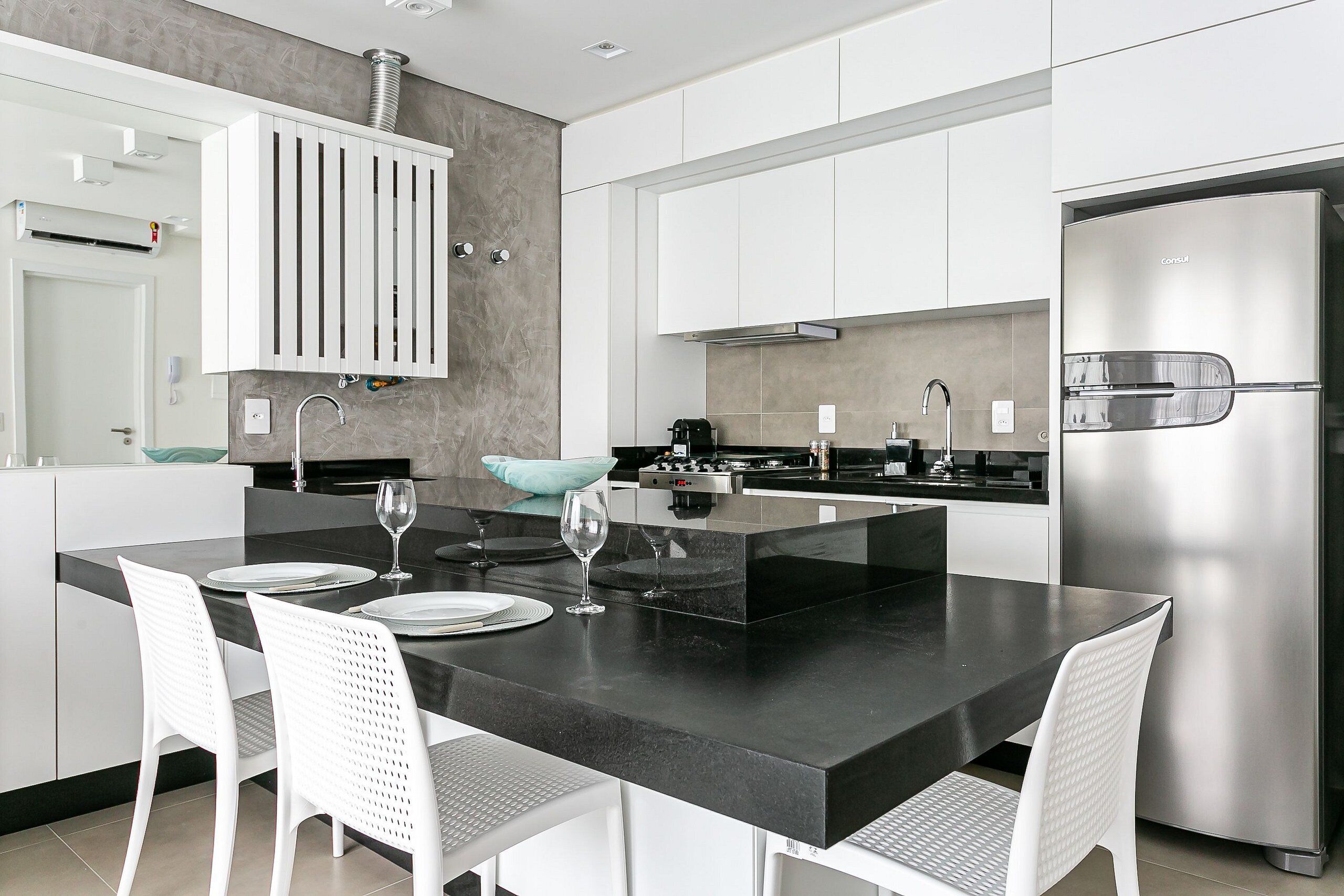 A modern kitchen with white cabinets, a stainless steel refrigerator, and a black countertop island with white chairs.